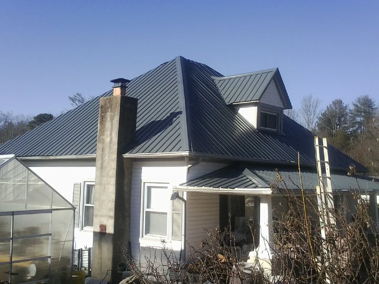 Dark blue standing seam metal roof on a white farmhouse with dormer — Slate & Tile Roof Repair by Roofing Brothers in Stanhope