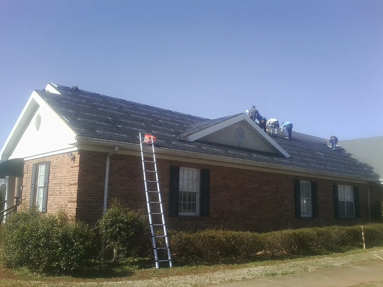 Crew tearing shingles off a brick ranch roof with a ladder set — Emergency Roof Repair work by our crew in Stanhope