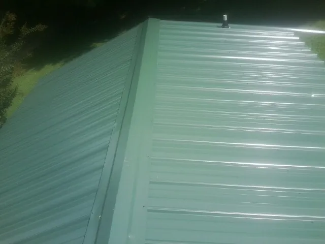 New green metal panels meeting at the ridge of a roof — Flat Roof Repair work by our crew in Stanhope